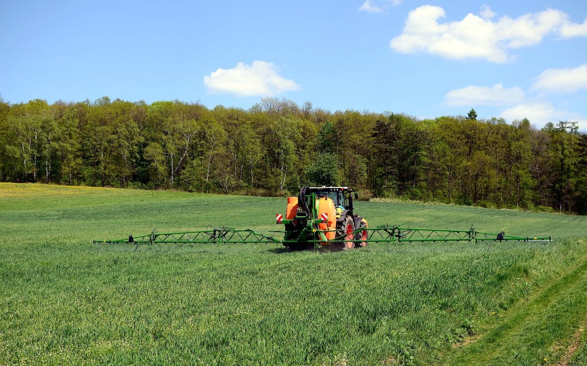Pflanzenschutzmittel wird ausgebracht auf einem Feld, im Hintergrund ein mitteleuropäischer Wald